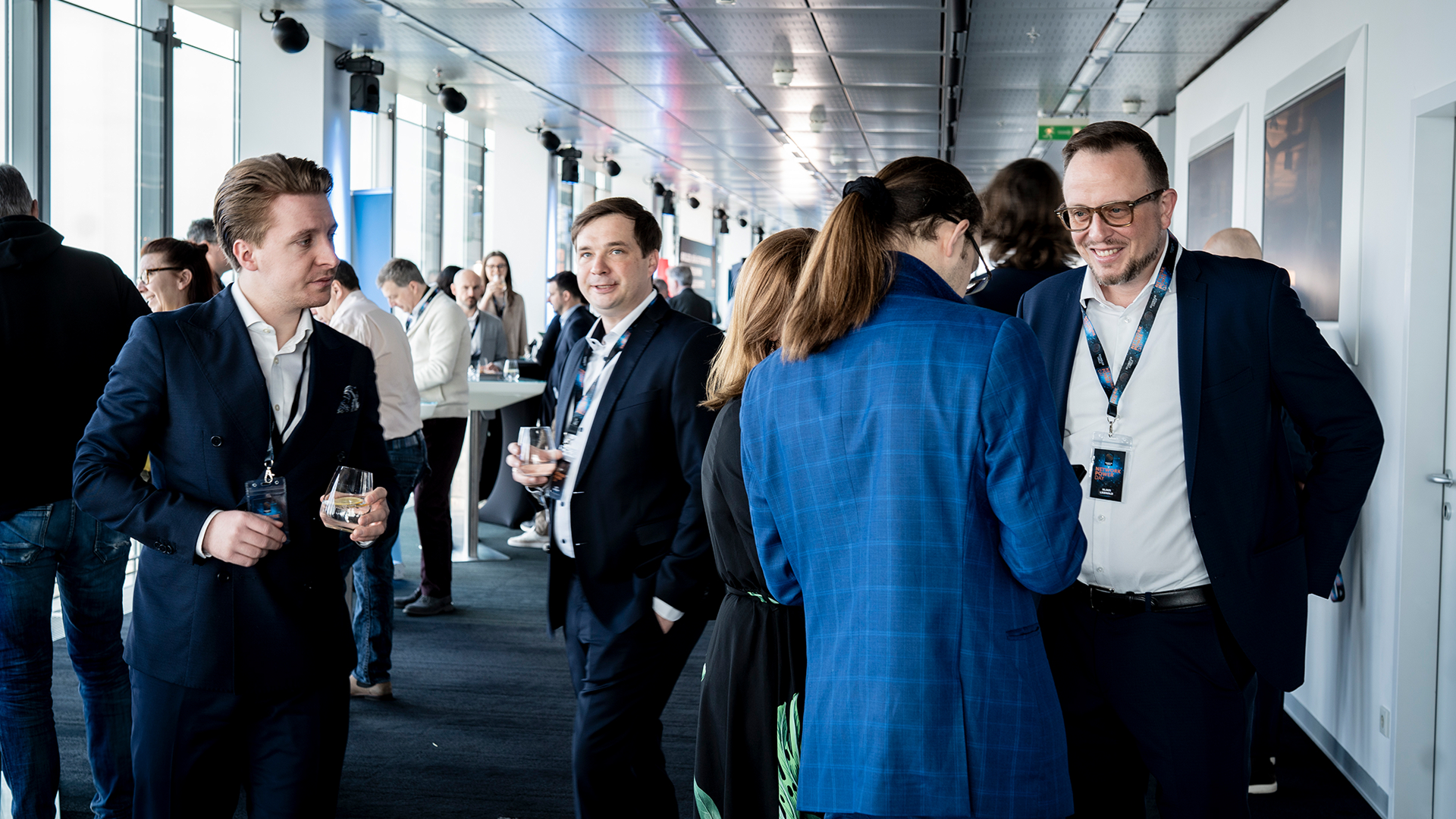 Business professionals socializing at a networking event. Men in suits and women in formal attire hold drinks, engaging in lively conversation.